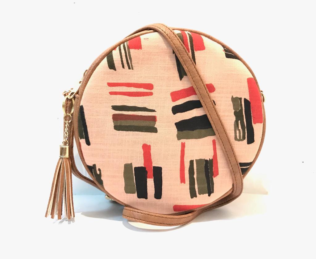 Round crossbody bag in blush pink with abstract brushstroke print in coral olive and black, tan leather trim