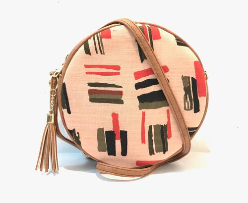 Round crossbody bag in blush pink with abstract brushstroke print in coral olive and black, tan leather trim