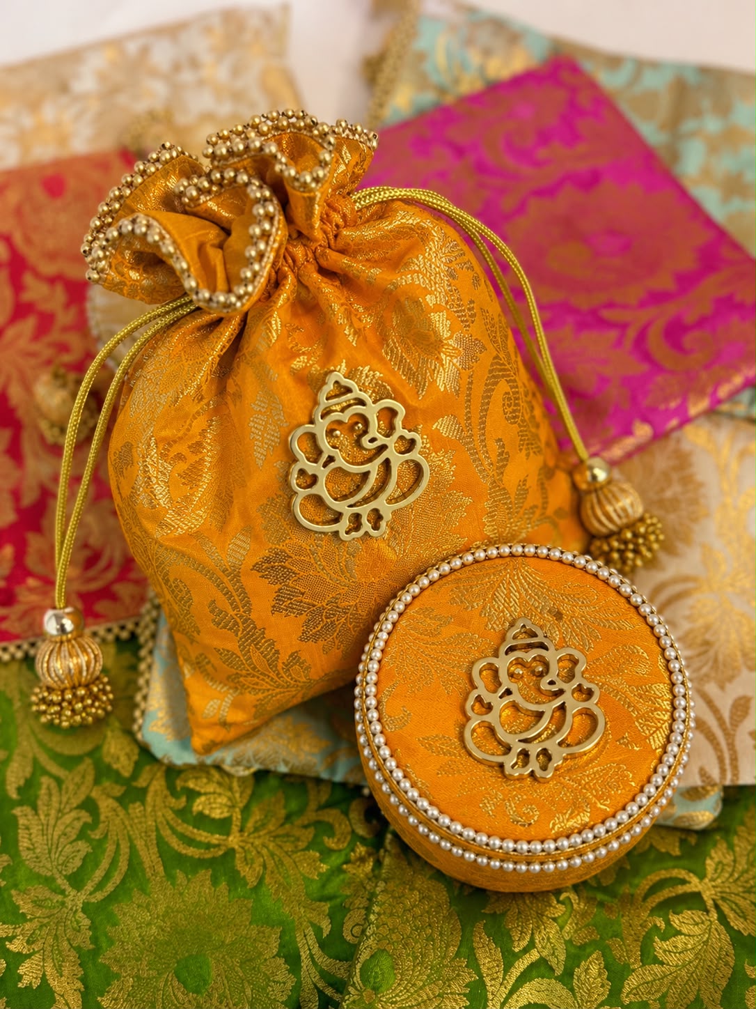 Mustard gold Banarasi brocade potli and box combo with gold Ganesha motif and tassels by Sache