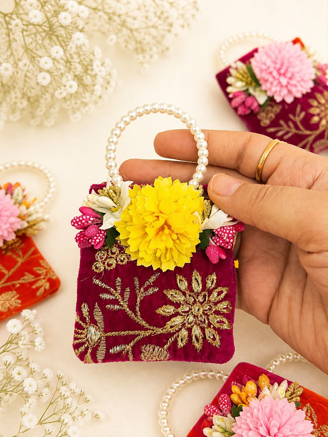 Rani pink velvet coin potli with gold zardozi floral embroidery, yellow fabric flower and pearl handle, a Sache Golu return gift