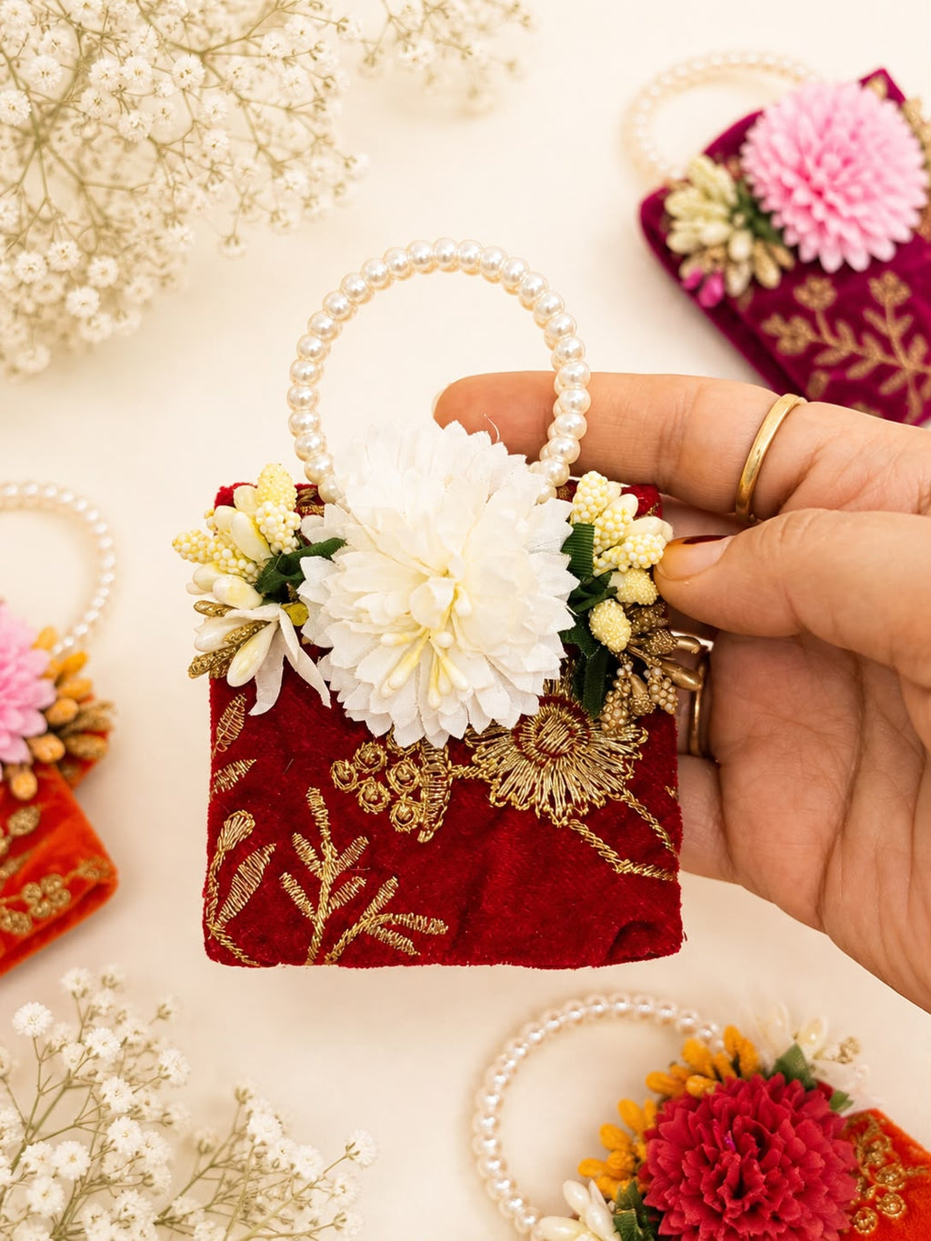 Deep red velvet coin potli with gold zardozi goldwork, white fabric flower and pearl beaded handle by Sache