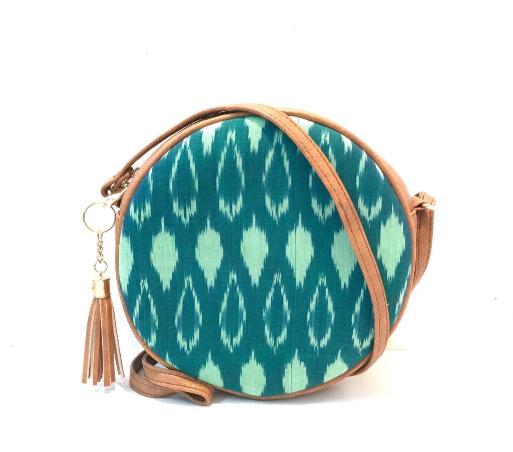 Round crossbody bag with vibrant teal and mint ikat print, tan leather trim and gold tassel zipper